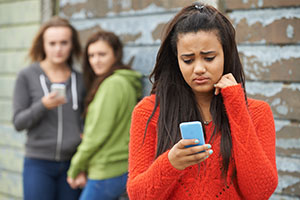Girl looking at her phone sad and other girls smiling behind her
